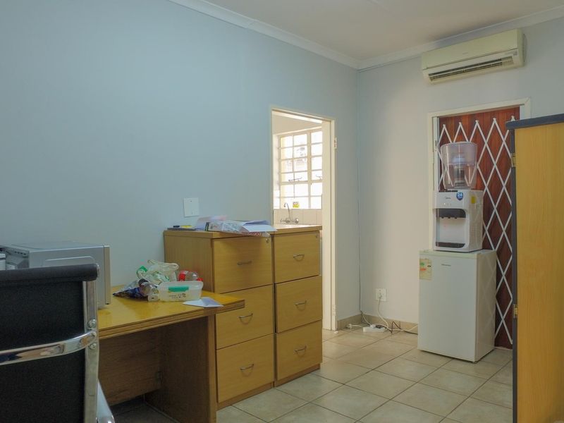 A functional office space featuring tiled flooring, a wall-mounted air conditioning unit, and a secure entrance door with a security gate.