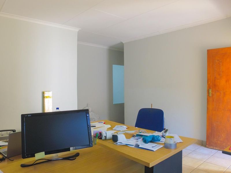 A functional office space featuring tiled flooring, neutral walls, and a wooden door, providing a practical environment for professional work.