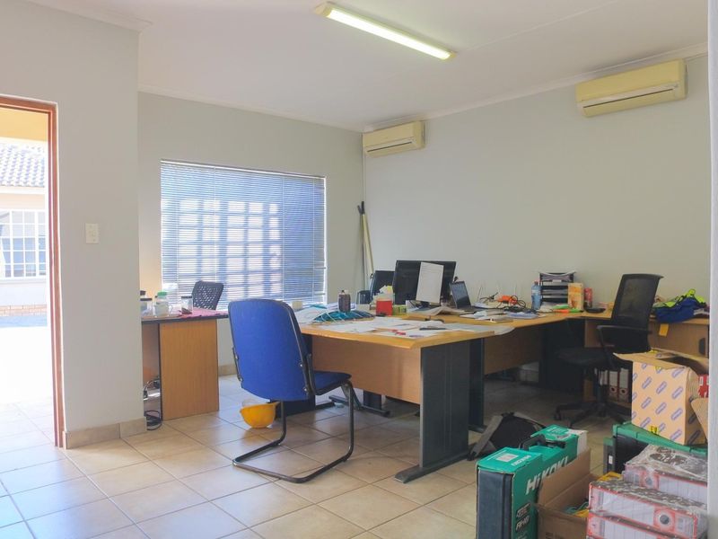 A functional office space featuring tiled flooring, dual split-system air conditioning units, and natural light through venetian blinds with direct access to an outdoor area.