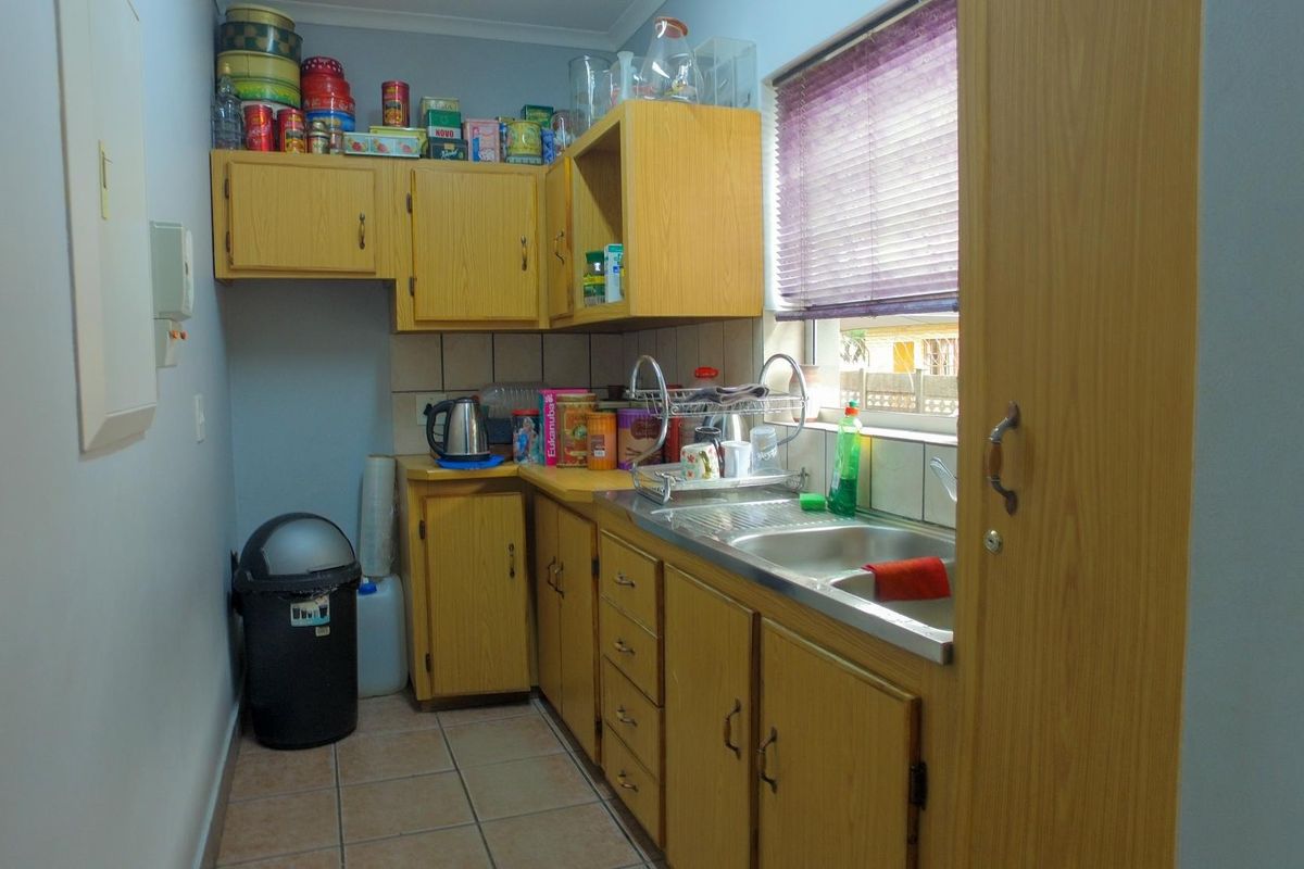 A compact kitchen featuring dated laminate cabinetry, a stainless steel sink, tiled backsplash, and tiled flooring, offering potential for a modern renovation.