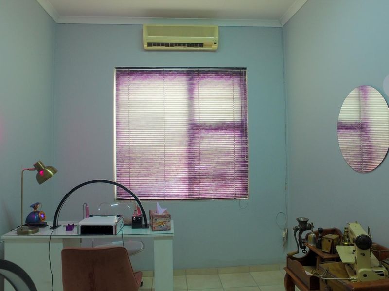 A functional office space featuring tiled flooring, a wall-mounted air conditioning unit, and a window fitted with venetian blinds.
