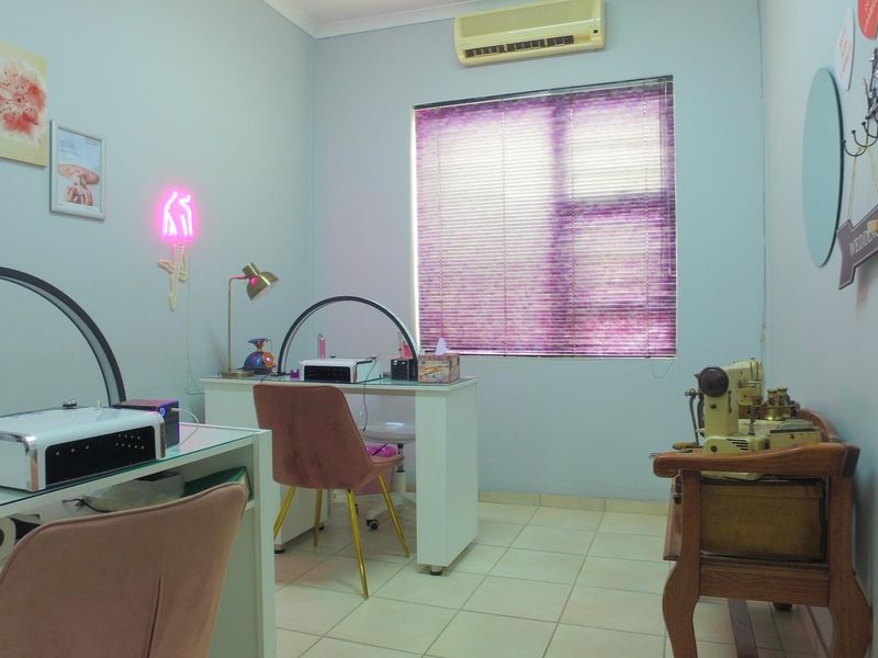 A functional office space featuring tiled flooring, a wall-mounted air conditioning unit, and window blinds, currently utilized as a beauty treatment room.