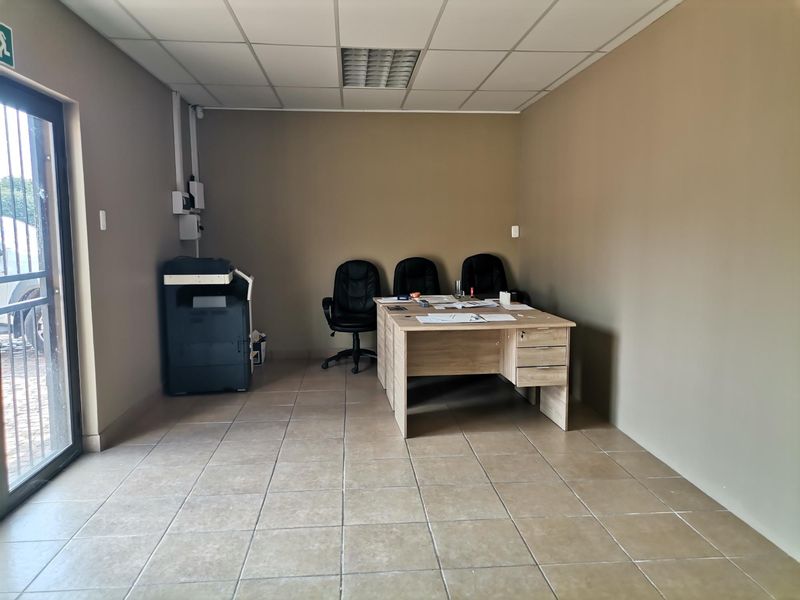 A functional office space featuring tiled flooring, a suspended ceiling with recessed lighting, and a secure glass entrance door.