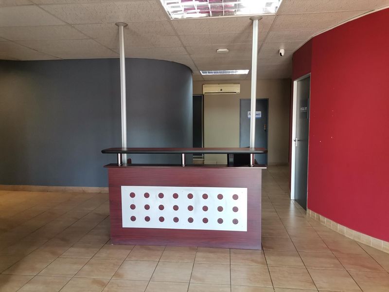 Office reception area featuring a built-in desk, ceramic tiled flooring, suspended ceiling, and wall-mounted air conditioning unit.