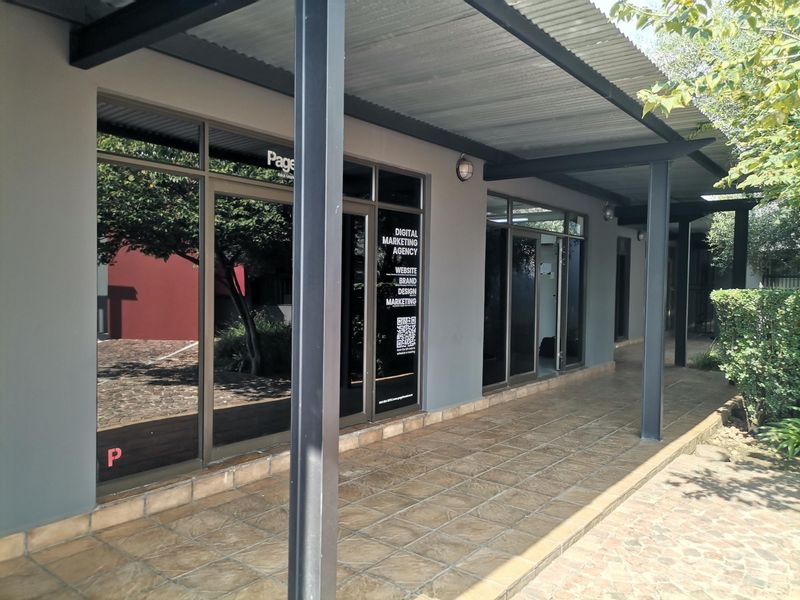 Front exterior view of an office unit featuring a covered walkway with tiled flooring and large aluminium-framed glass entrance doors.