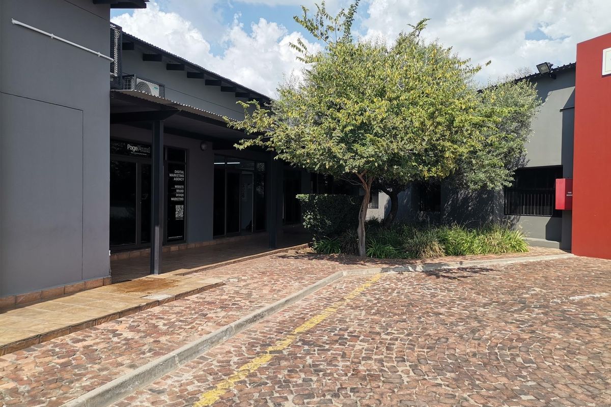 Exterior view of a modern office complex featuring a cobblestone driveway, covered walkways, and glass-fronted office units.