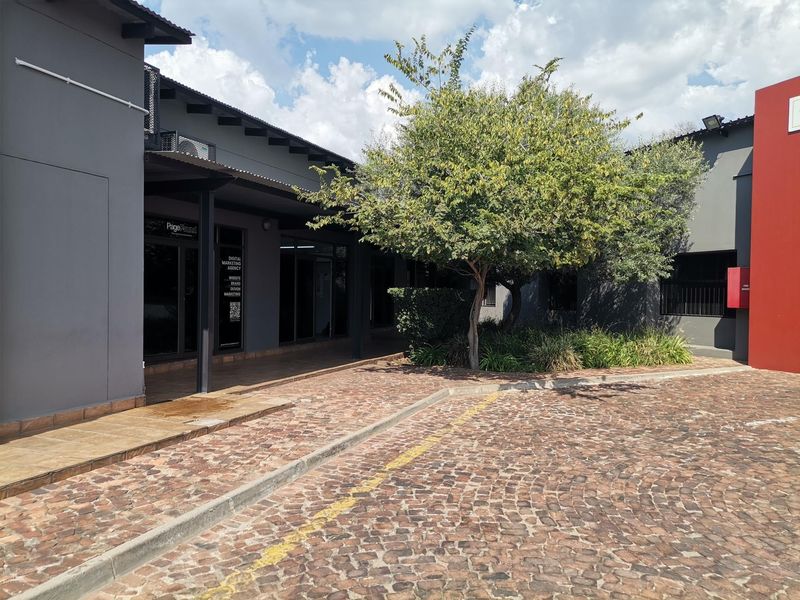 Exterior view of a modern office complex featuring a cobblestone driveway, covered walkways, and glass-fronted office units.