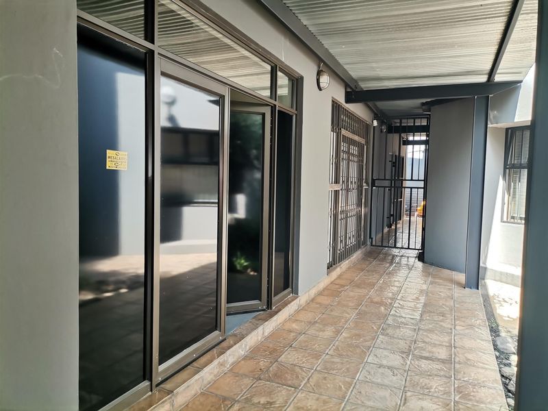 A covered outdoor patio area featuring tiled flooring, aluminium sliding doors, and a secure metal gate, providing a clean and functional transition space.
