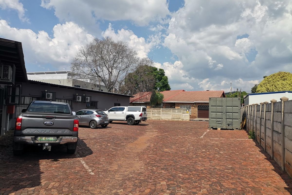 A paved rear parking area featuring a secure perimeter wall, gated access, and exterior-mounted air conditioning units on the building facade.