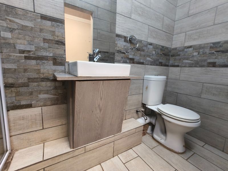A compact bathroom featuring a vessel sink on a wooden vanity, a standard toilet, and decorative stone-effect wall tiling.