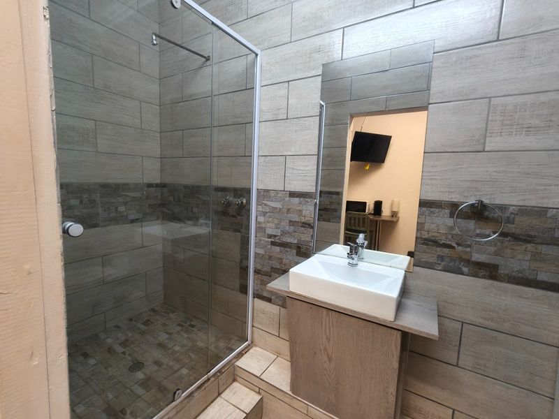 Modern bathroom featuring a glass-enclosed shower, vessel sink with vanity cabinet, and contemporary tiled walls.