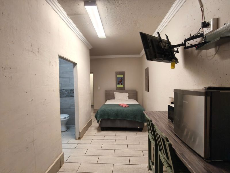 A compact bedroom featuring tiled flooring, cove cornicing, and an en-suite bathroom access, providing a functional guest accommodation space.