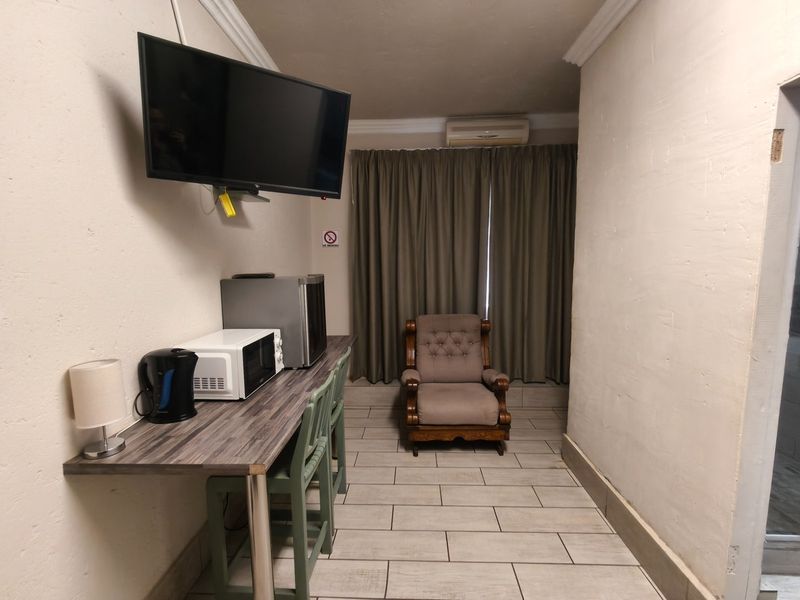 A compact bedroom featuring tiled flooring, a wall-mounted television, air conditioning, and a built-in desk area with neutral finishes.