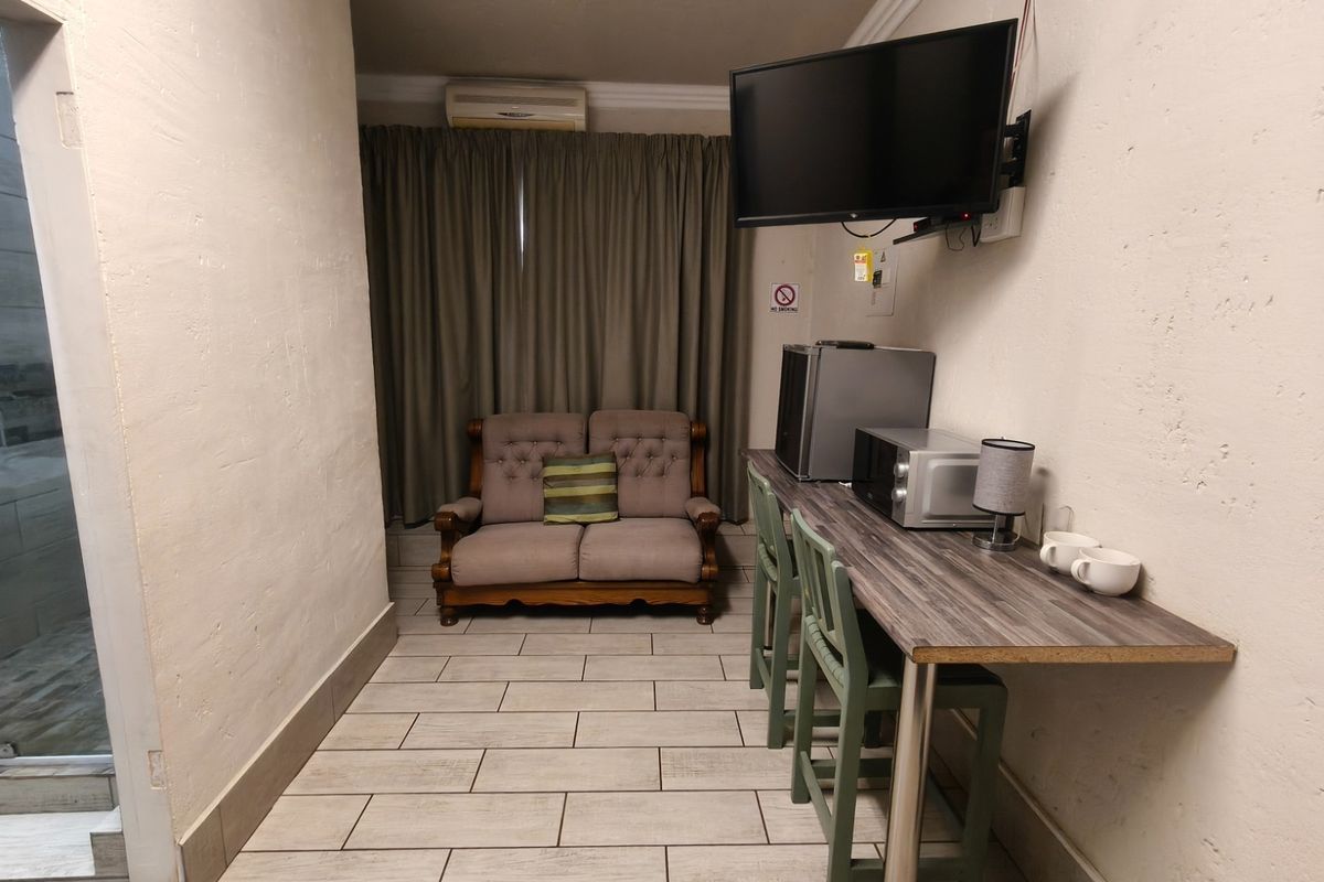 A compact living area featuring tiled floors, a wall-mounted television, and a built-in breakfast bar counter, suitable for guest house accommodation.
