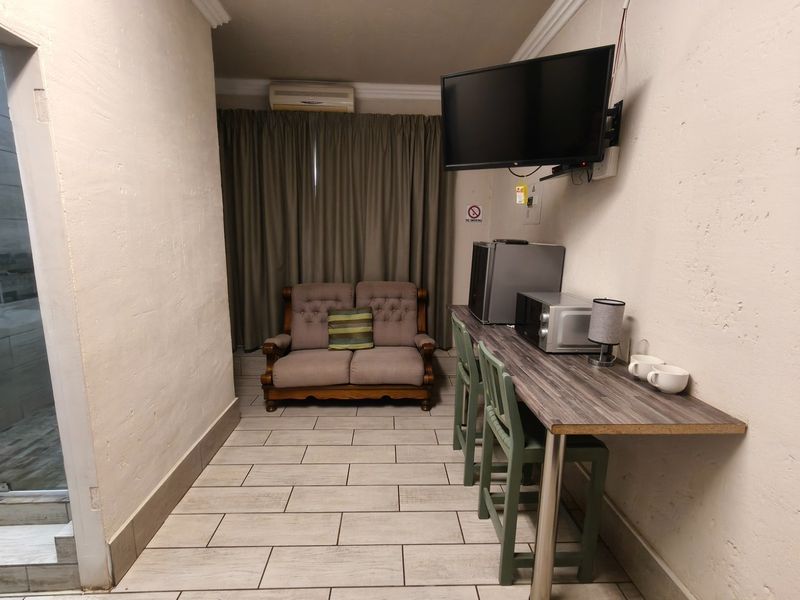 A compact living area featuring tiled floors, a wall-mounted television, and a built-in breakfast bar counter, suitable for guest house accommodation.