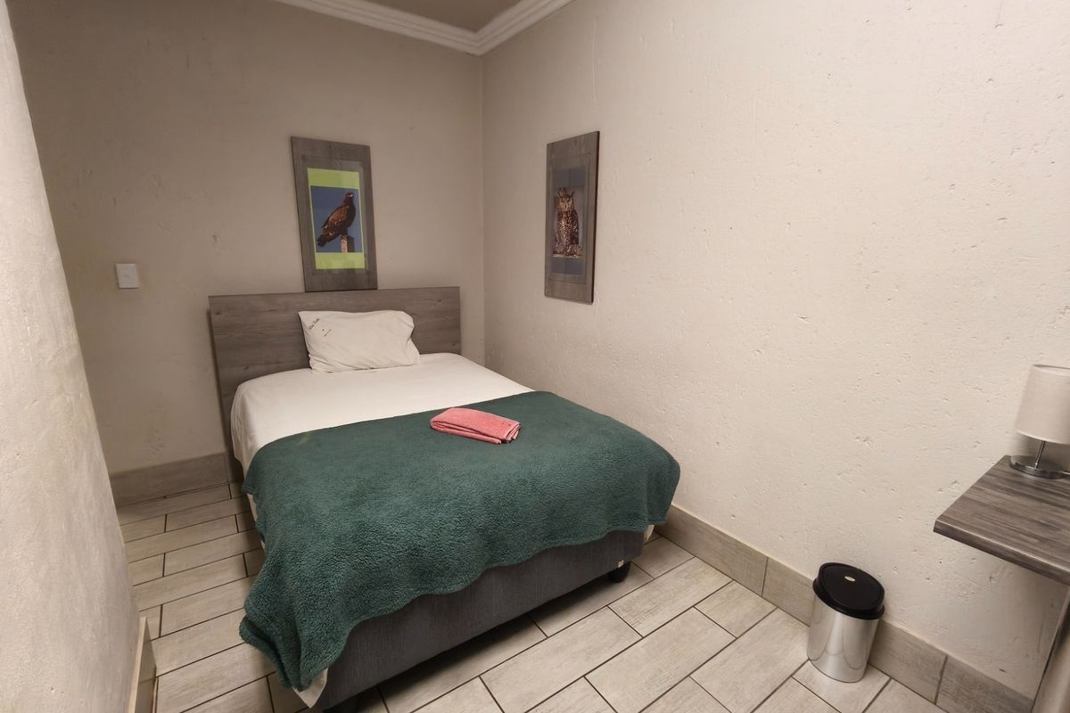 A compact bedroom featuring tiled flooring, crown molding, and a built-in wall shelf, providing a functional space for guests.