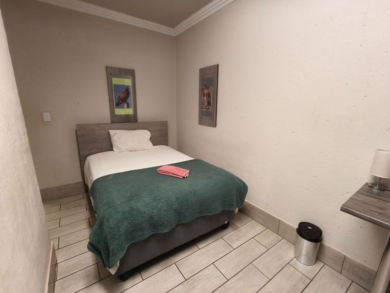A compact bedroom featuring tiled flooring, crown molding, and a built-in wall shelf, providing a functional space for guests.