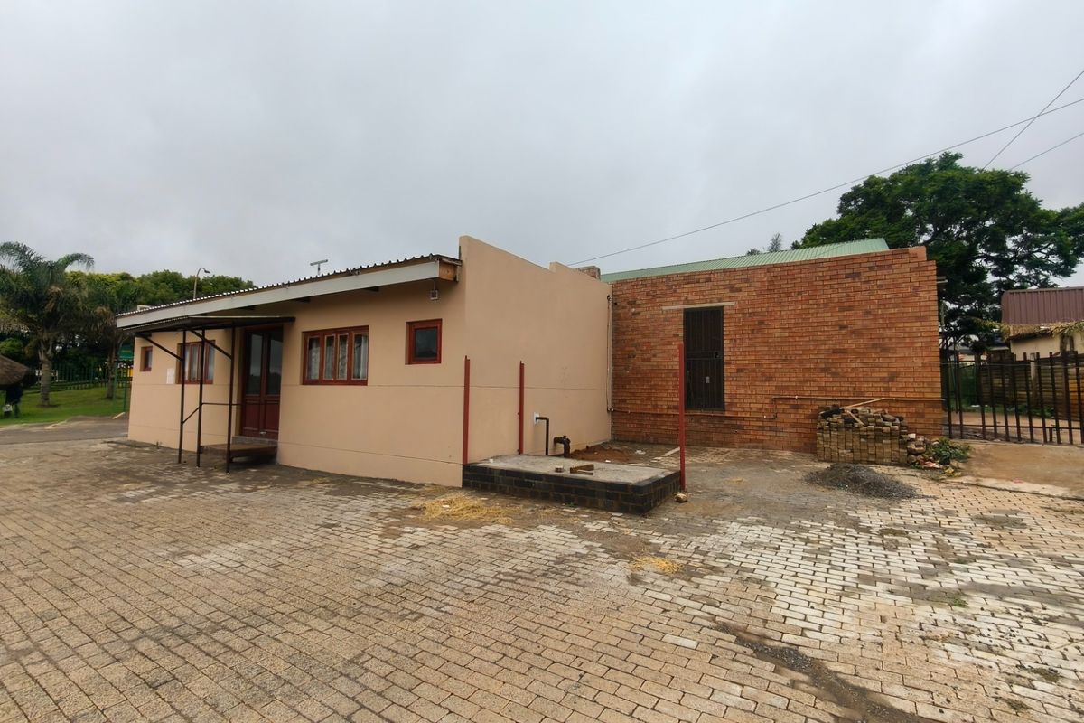 Rear exterior view of the guest house showing a mix of plastered and brick finishes with an unfinished paved area and exposed plumbing.