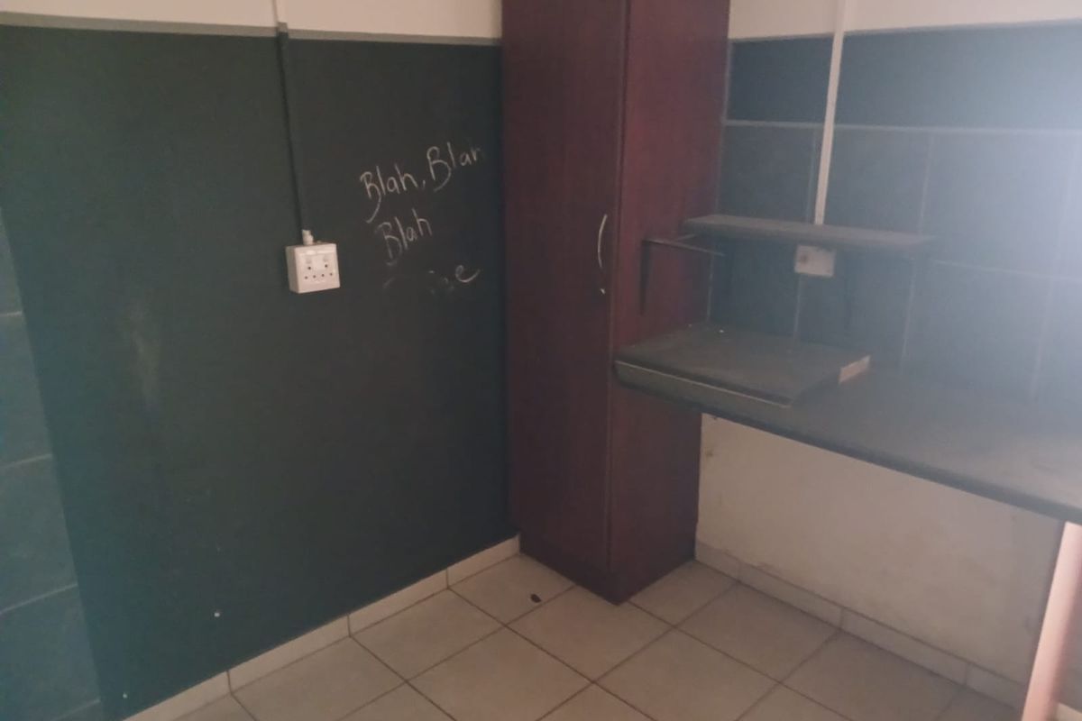 A small, empty kitchen area featuring tiled floors, wall tiling, and built-in cabinetry, currently requiring cosmetic updates and cleaning.