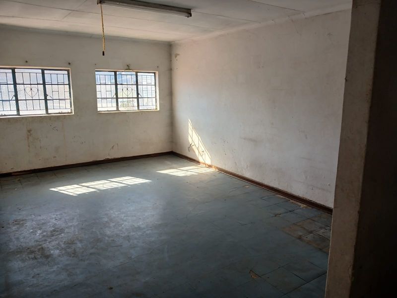 An empty, industrial-style office space featuring tiled flooring, security bars on windows, and basic overhead lighting, requiring cosmetic updates.