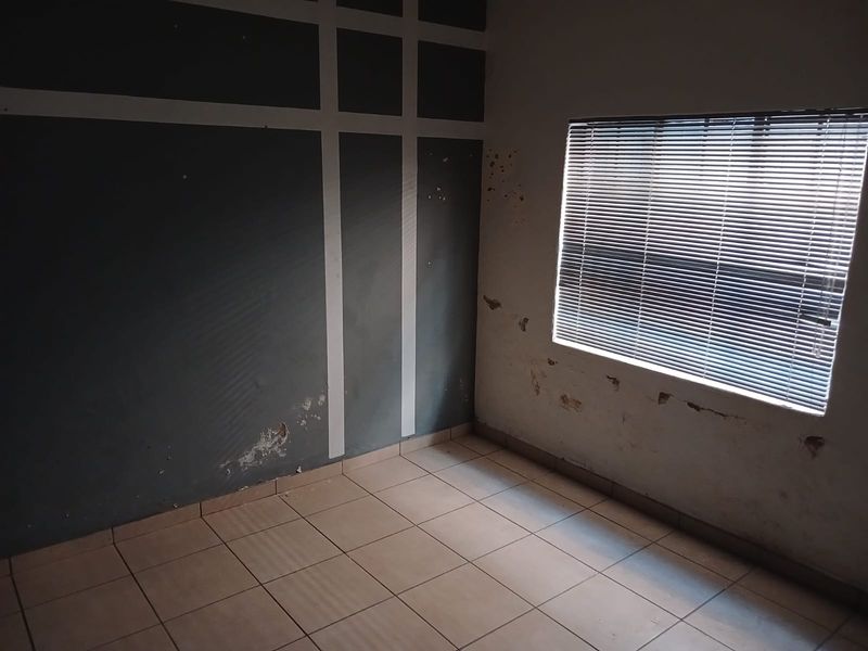 An empty bedroom featuring tiled flooring and venetian blinds, currently requiring wall repairs and repainting to restore the space.