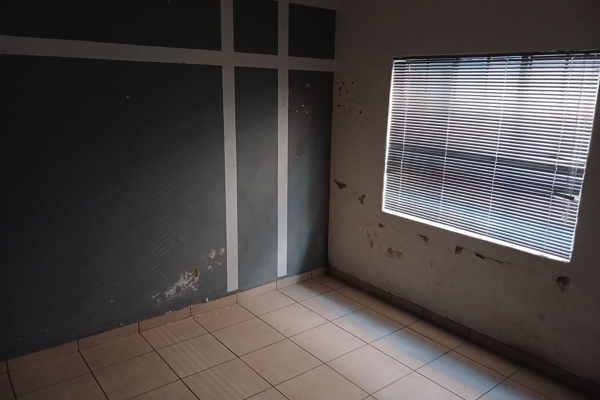 An empty bedroom featuring tiled flooring and venetian blinds, currently requiring wall repairs and repainting to restore the space.