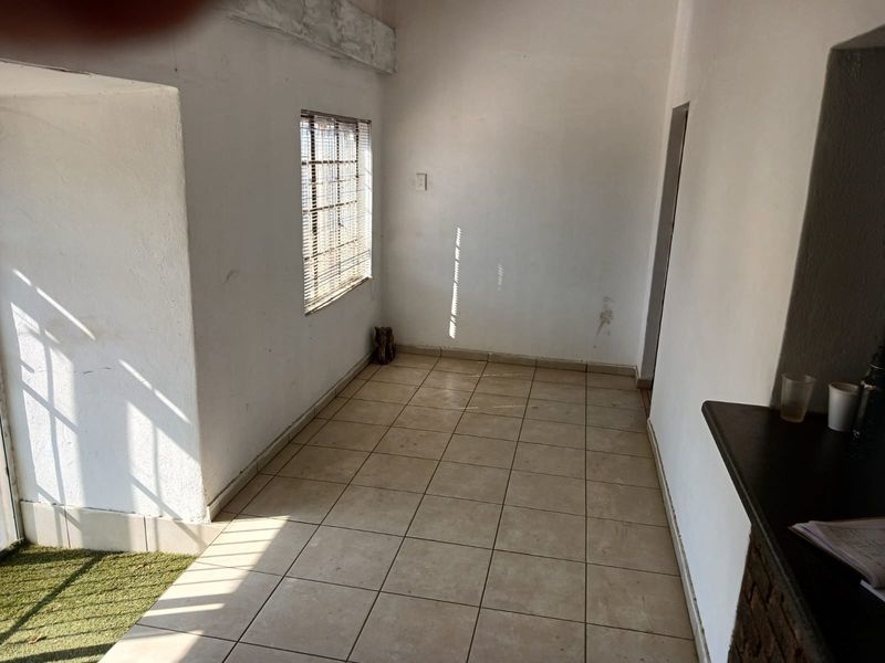 An empty, sunlit interior space featuring tiled flooring, security bars on the window, and a built-in counter, suitable for a living or utility area.