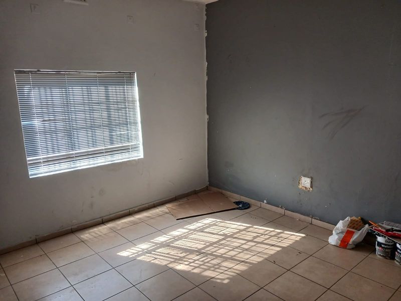 An empty bedroom featuring tiled flooring, a window with venetian blinds, and dual-tone painted walls requiring minor cosmetic attention.