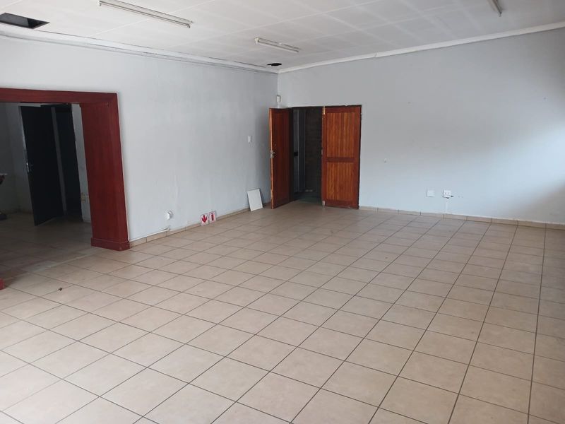 An empty, open-plan industrial office space featuring tiled flooring, suspended ceilings, and multiple wooden door access points.