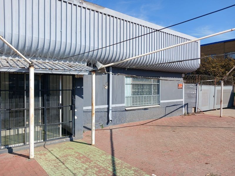 Front exterior view of an industrial property featuring corrugated metal cladding, security bars, and a paved driveway area.