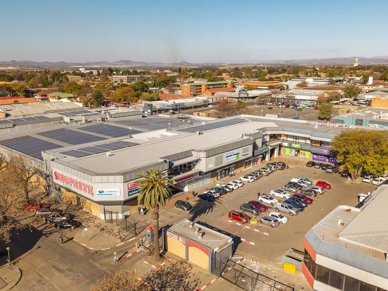Aerial view of a commercial shopping center featuring a large roof with solar panels, an adjacent parking lot, and surrounding urban infrastructure.