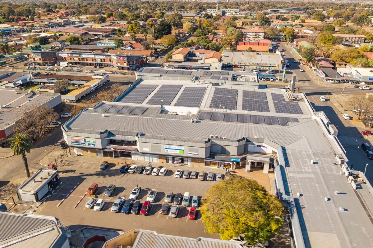 Aerial view of a commercial shopping center featuring extensive rooftop solar panel installations and an adjacent paved parking area.