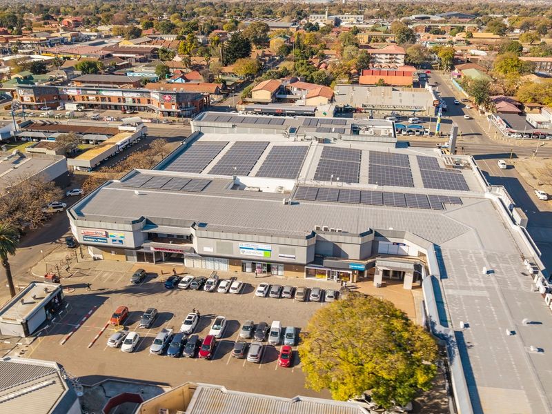 Aerial view of a commercial shopping center featuring extensive rooftop solar panel installations and an adjacent paved parking area.