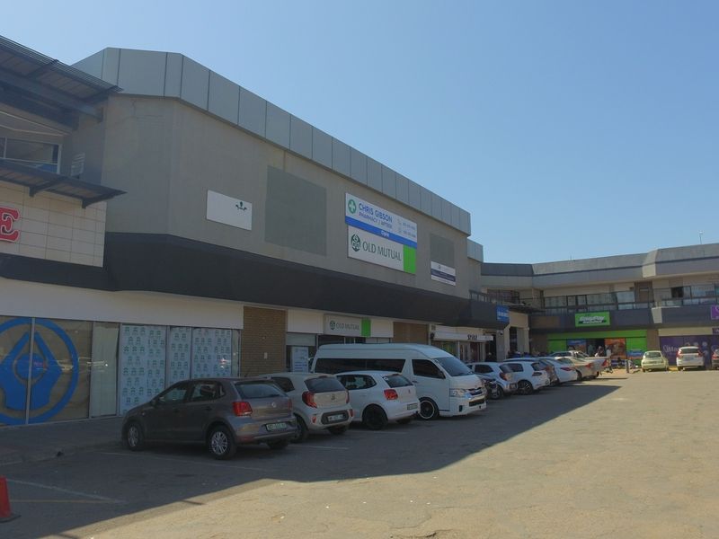 Exterior view of a commercial shopping center featuring multiple storefronts, building signage, and an adjacent paved parking lot.