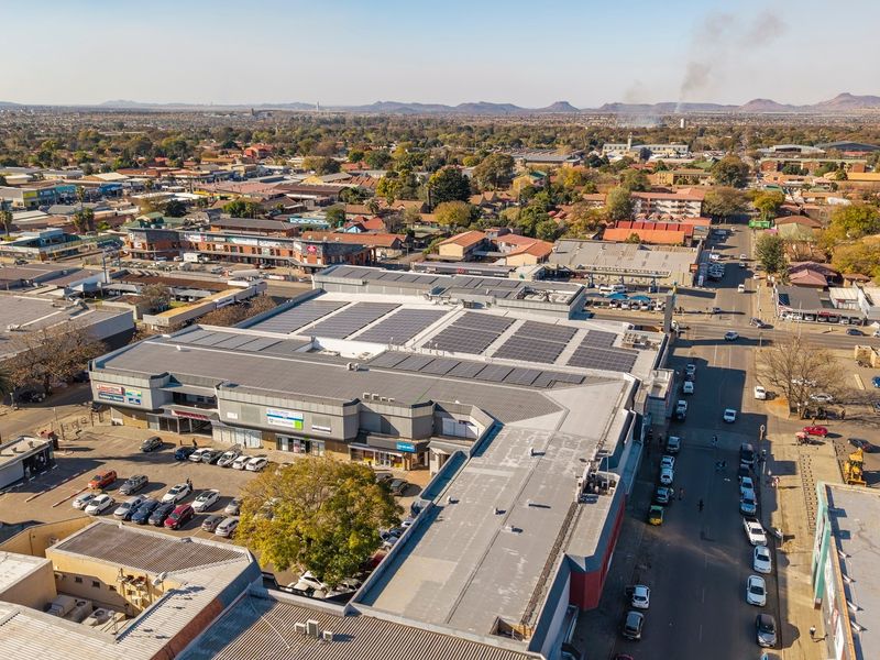 Aerial view of a commercial shopping center featuring extensive rooftop solar panel installations and an adjacent parking area within a busy urban environment.