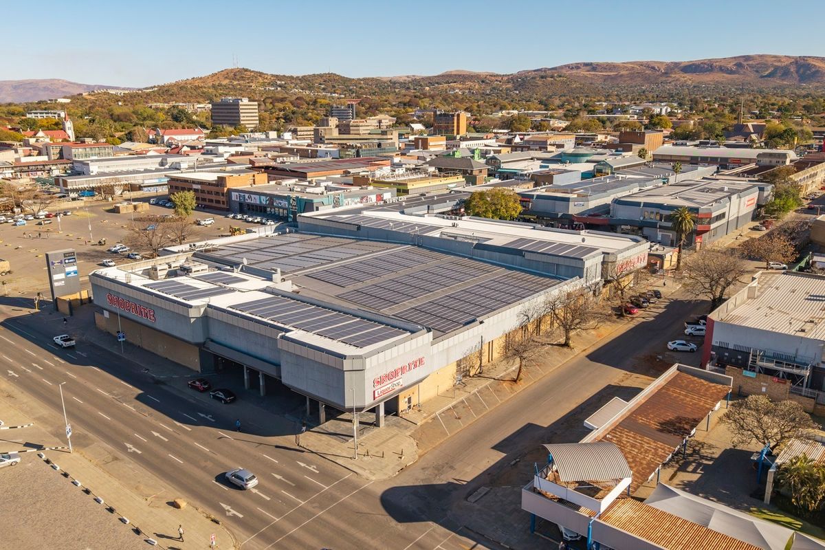 Aerial view of a commercial retail property featuring a large roof-mounted solar array, situated within a busy urban street and retail district.