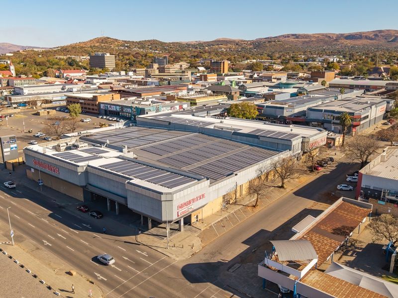 Aerial view of a commercial retail property featuring a large roof-mounted solar array, situated within a busy urban street and retail district.