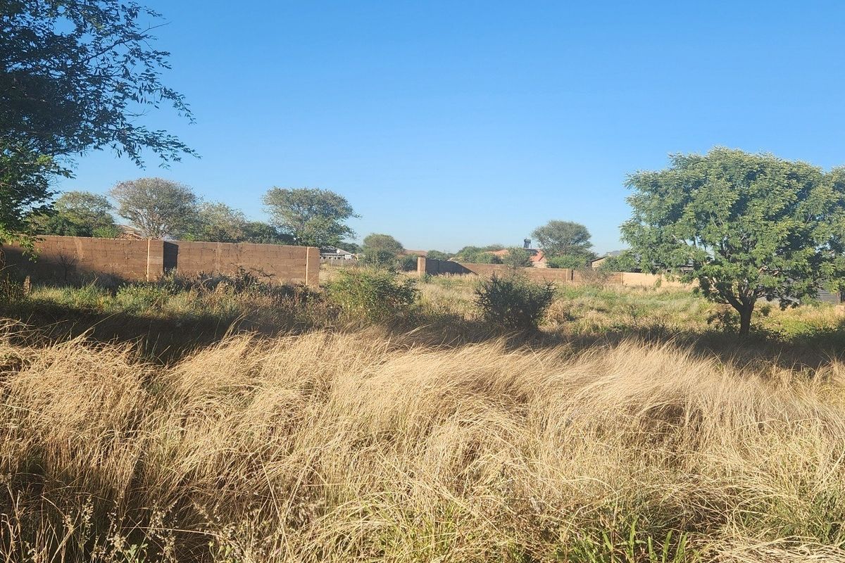 A view of a vacant commercial land plot featuring established perimeter boundary walls and mature trees, offering a clear space for future development.