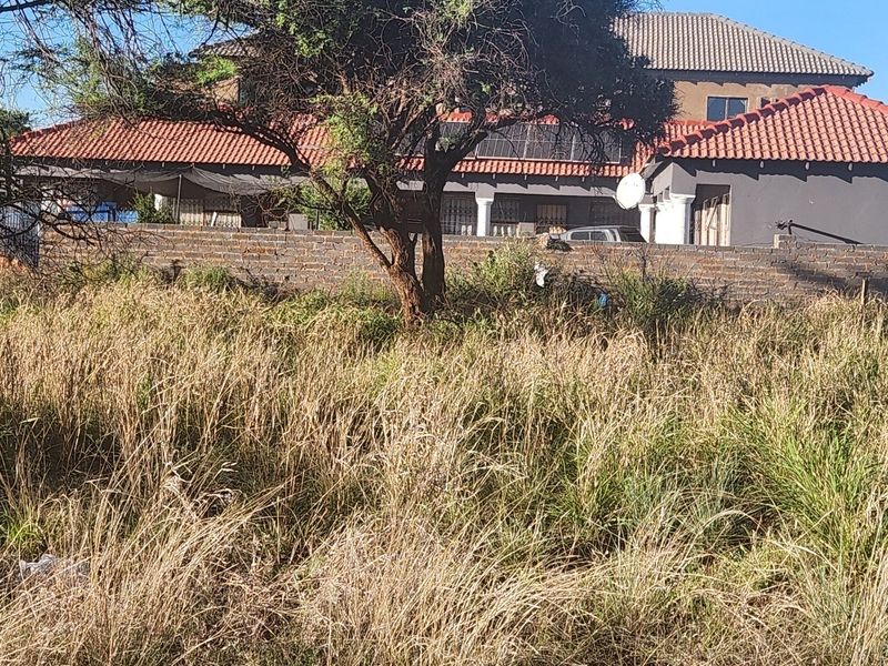 View of a vacant commercial plot with a brick boundary wall and an adjacent residential building in the background.