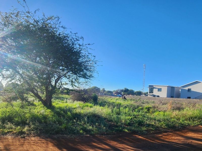 A view of a vacant commercial land plot featuring natural vegetation, perimeter fencing, and a nearby telecommunications tower.