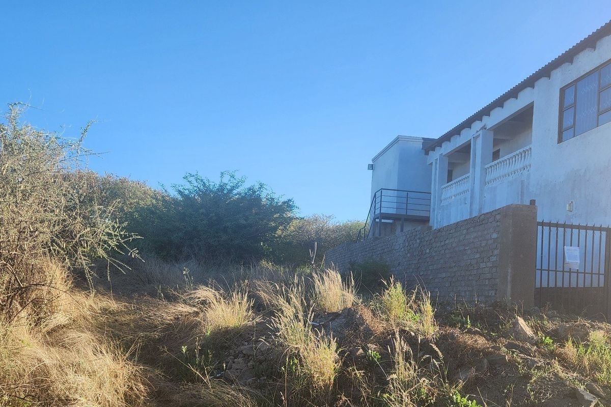 Rear view of the property showing a multi-level structure with a balcony, external staircase, and brick boundary wall set against an overgrown garden area.