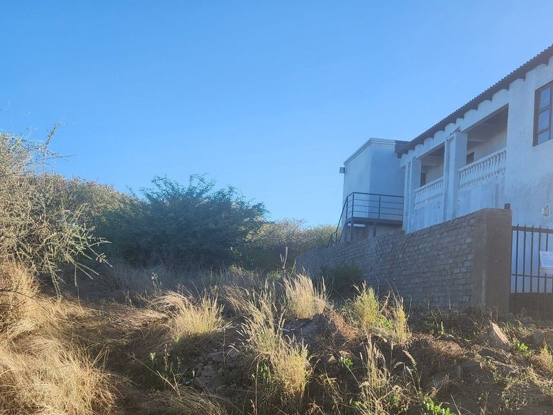 Rear view of the property showing a multi-level structure with a balcony, external staircase, and brick boundary wall set against an overgrown garden area.