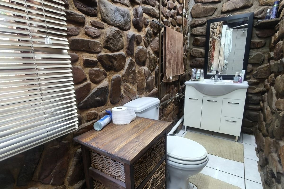 A rustic bathroom featuring distinctive natural stone wall cladding, a modern white vanity cabinet, and tiled flooring.