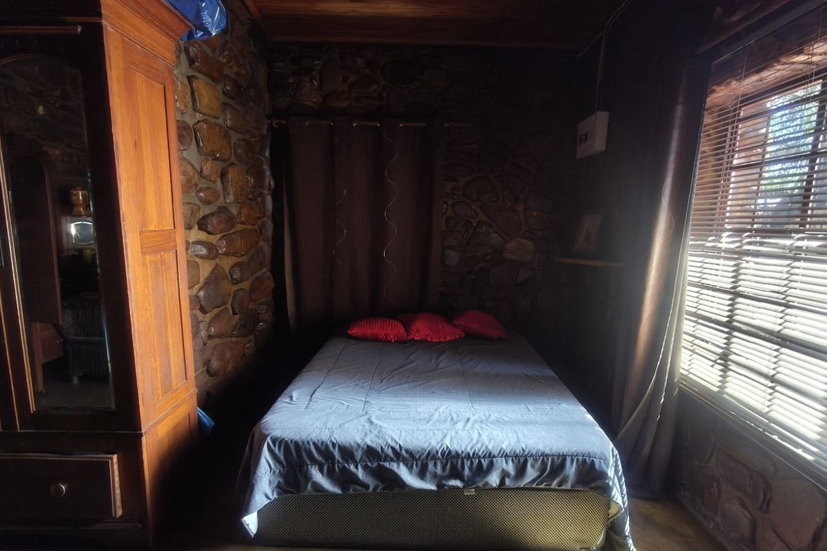 A rustic bedroom featuring distinctive stone wall cladding and a timber ceiling, complemented by natural light through venetian blinds.