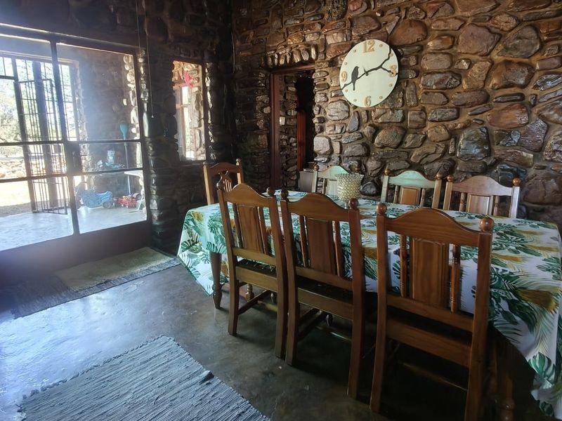 Rustic dining room featuring exposed stone masonry walls, polished concrete flooring, and large glass doors providing natural light and access to the exterior.