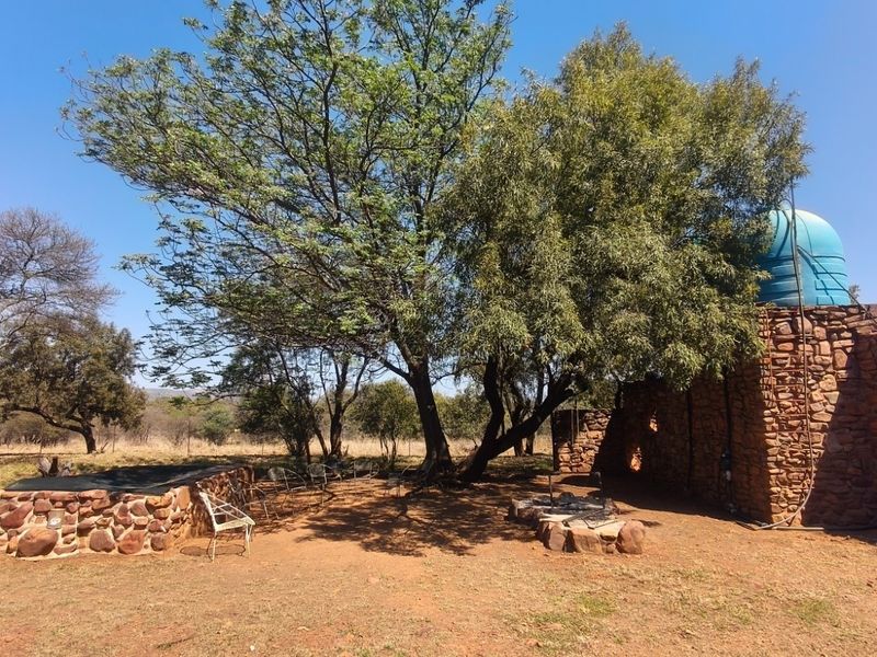Outdoor area featuring a stone masonry wall, a water storage tank, and a built-in stone fire pit set within a natural farm landscape.