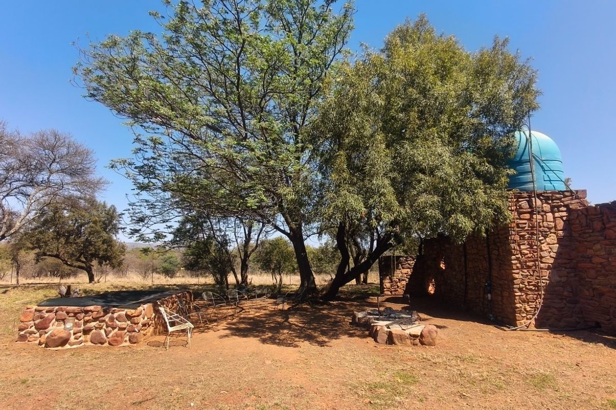 Outdoor area featuring a stone masonry wall, a water storage tank, and a built-in stone fire pit set within a natural farm landscape.