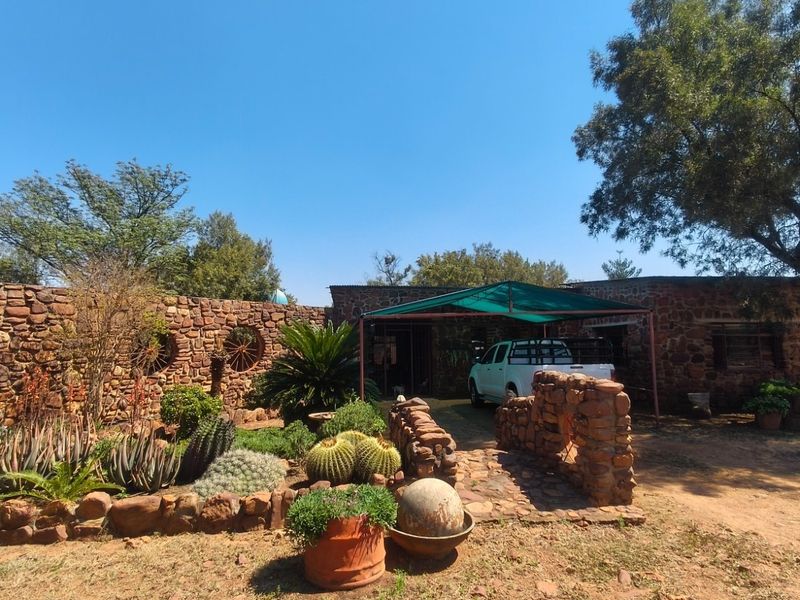 A rustic farm-style property featuring distinctive stone masonry walls, a landscaped garden with desert-style plantings, and a covered carport area.