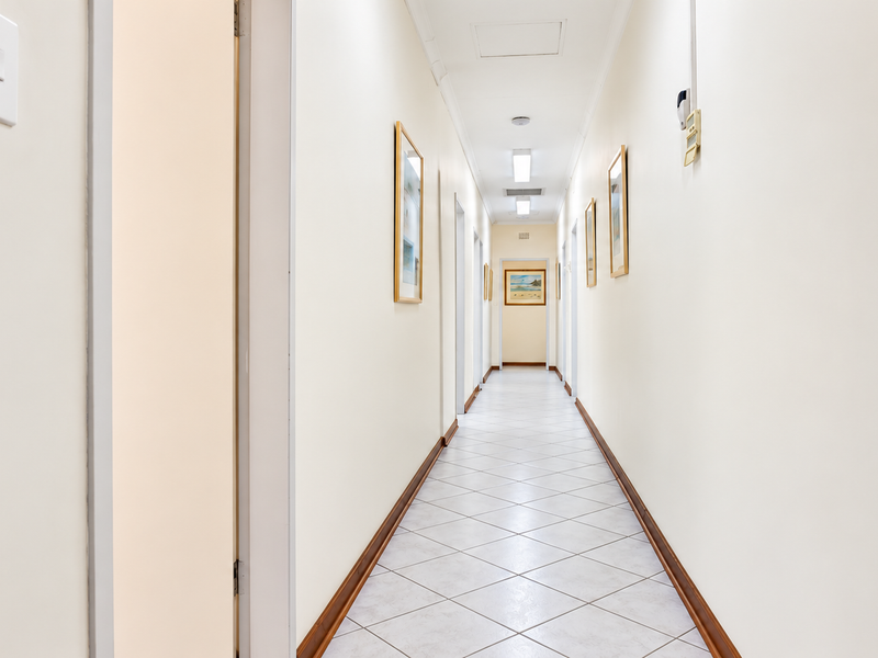 A clean and well-maintained office hallway featuring neutral tiled flooring, recessed lighting, and multiple access points to surrounding office spaces.