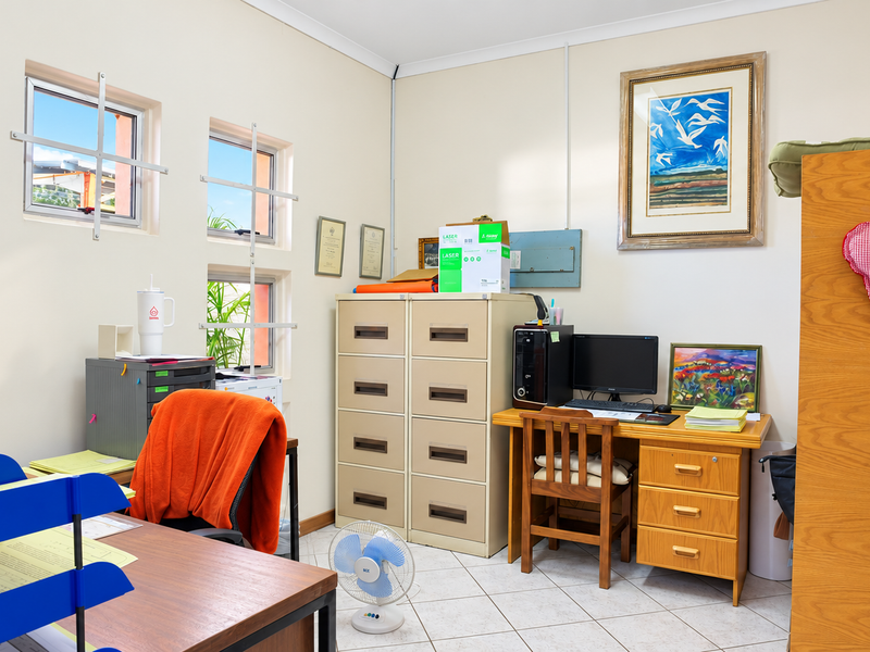A functional office space featuring tiled flooring and windows equipped with security bars, providing a practical work environment.